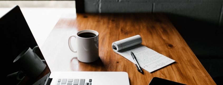 MacBook Pro, white ceramic mug,and black smartphone on table