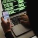 Free Unrecognizable hacker with smartphone typing on laptop at desk Stock Photo