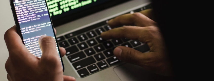 Free Unrecognizable hacker with smartphone typing on laptop at desk Stock Photo